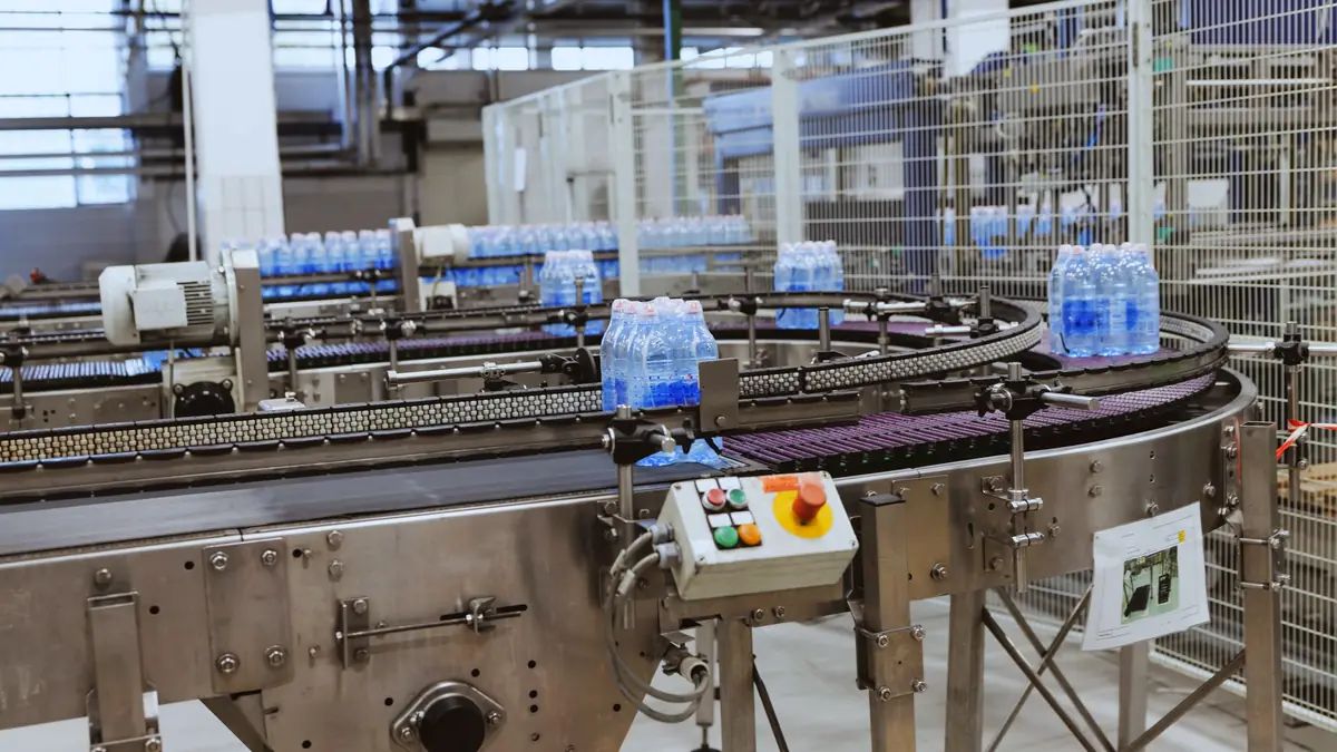 Running PET bottled water line with shrink-wrapped bottle packs moving on stainless steel conveyors